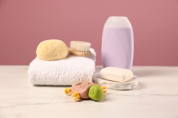 Baby accessories and bathing products on white marble table against pink background, closeup