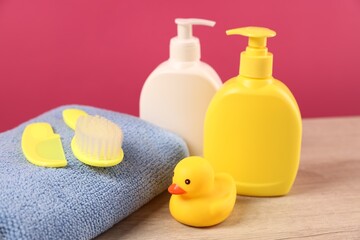 Baby accessories and bathing products on wooden table against pink background, closeup