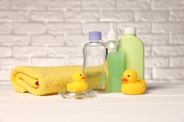 Baby accessories and bathing products on white wooden table near brick wall