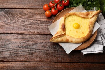 Tasty khachapuri with cheese, egg, tomatoes and parsley on wooden table, flat lay. Space for text
