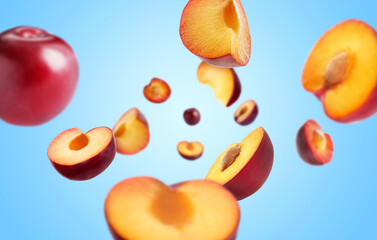 Fresh ripe plums swirling in air against light blue background