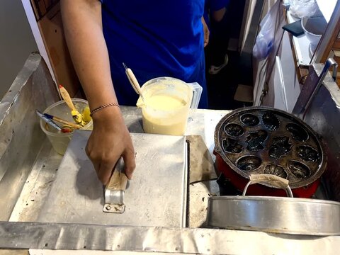 A food vendor is cooking kue cubit or a sweet pancake, on a frying pan. Kue cubit is a Betawi Indonesian specialty. It's made from flour, milk, and chocolate sprinkles