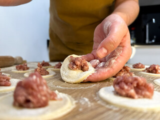 Making dumplings with raw meat filling on floured kitchen table close-up, traditional homemade cooking preparation process, lifestyle food background, no people visible
