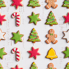 Colorful seamless pattern with Christmas cookies shaped like trees, stars, gingerbread men, and candy canes on white wooden background