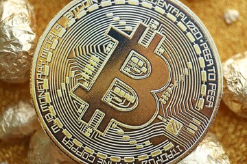 Small pile of golden nuggets and bitcoin cryptocurrency coin on shiny gold glitter background