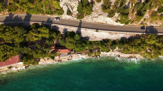 Cinematic aerial top view sliding left above Adriatic highway showing cars shadows seaside pines rocky beach and crystal water