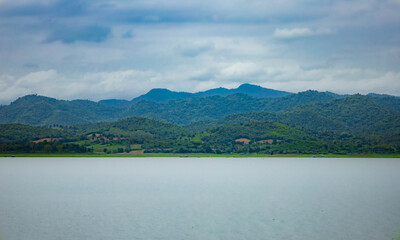 Obraz premium A peaceful rural scene in the dam featuring a green mountain with cloudy sky Srinagarindra national park, Kanchanaburi, Thailand.