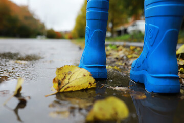 legs of child in blue rubber boots jumping in the autumn puddles