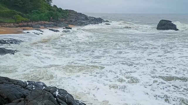 footage of ocean waves gently crashing against tetrapod rock barriers on a serene beach. Ideal for background, nature, travel, or environmental themes with calm sea and sandy shoreline.