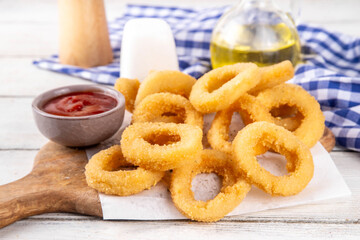 Golden onion rings with ketchup sauce, airfryer cooked tasty onion ring snacks on white wooden table copy space