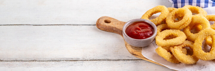 Golden onion rings with ketchup sauce, airfryer cooked tasty onion ring snacks on white wooden table copy space