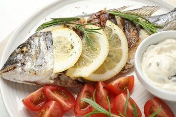 Tasty roasted dorado fish with sauce, tomatoes and lemon on white table, closeup. Homemade seafood dish
