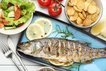 Tasty roasted seabass fish served with salad and potatoes on white wooden table, flat lay. Homemade seafood dish