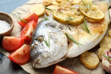 Tasty roasted dorado fish with vegetables and spices on table, closeup. Homemade seafood dish