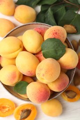 Fresh ripe apricots in bowl and green leaves on white table, flat lay