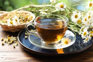 Tasty chamomile tea and flowers on wooden table, closeup