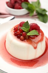 Delicious panna cotta with berries, sauce and mint on white table, closeup