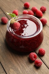 Tasty raspberry jam in glass jar on wooden table, closeup