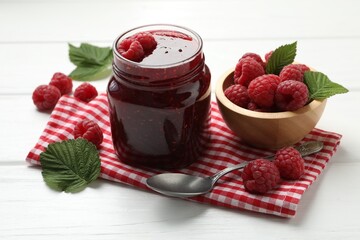 Tasty jam, fresh ripe raspberries and leaves on white wooden table, closeup