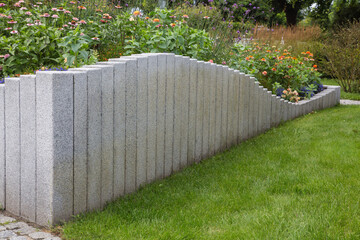 Modern Garden Design and Landscaping:Raised bed fenced by concrete blocks in different heights vertically erected-planted with flowers, perennial herbs-surrounded by grass, cobble and pebble stones