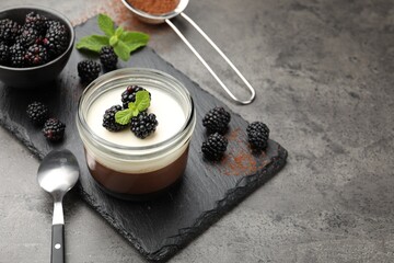 Tasty panna cotta with blackberries, mint and cocoa powder on grey table. Space for text
