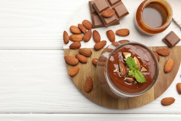 Delicious chocolate panna cotta with almonds, mint and caramel sauce on white wooden table, flat lay. Space for text