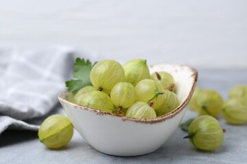 Fresh green gooseberries in bowl on grey table, closeup