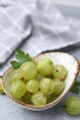 Fresh green gooseberries in bowl on grey table, closeup