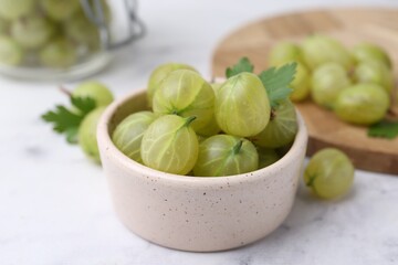 Fresh green gooseberries in bowl on white table, closeup