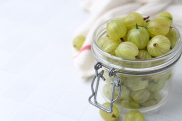 Fresh green gooseberries in jar on white table, closeup. Space for text