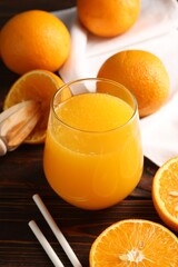 Fresh orange juice in glass, fruits, straws and juicer on wooden table, closeup