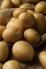 Many raw potatoes on burlap fabric, closeup