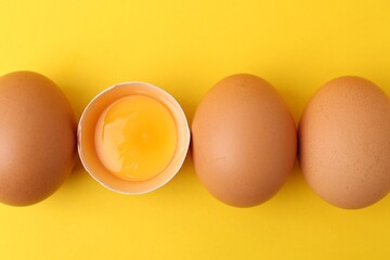 Whole and broken chicken eggs on yellow background, top view