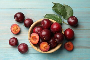Ripe cherry plums, bowl and green leaves on light blue wooden table, flat lay