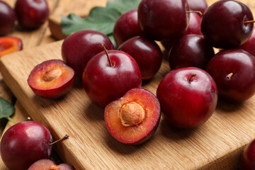 Whole, cut cherry plums and board on wooden table, closeup