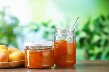 Tasty apricot jam and fresh fruits on wooden table against blurred background, closeup
