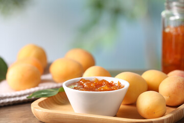 Tasty apricot jam and fresh fruits on wooden table against blurred background, closeup