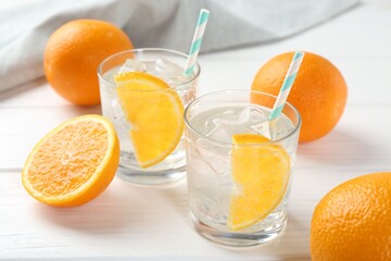 Sparkling water with orange slices in glasses and fresh fruits on white wooden table, closeup