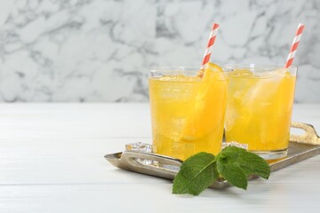 Refreshing soda water with orange slices in glasses and mint on white wooden table, closeup. Space for text