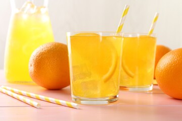 Refreshing soda water with orange slices in glasses, jug and fresh fruits on pink wooden table, closeup