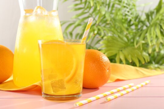 Refreshing soda water with orange slice in glass, jug and fresh fruits on pink wooden table, closeup