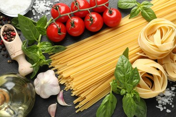 Different types of pasta and ingredients on black table, flat lay