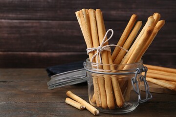 Delicious grissini sticks in open glass jar on wooden table, closeup