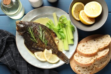 Tasty roasted flounder fish with celery served on blue wooden table, flat lay. Homemade seafood dish