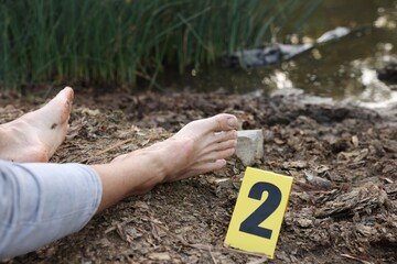 Forensic expertise. Crime scene with dead man's body and marker outdoors, closeup