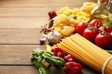 Different types of raw pasta and products on wooden table, closeup. Space for text