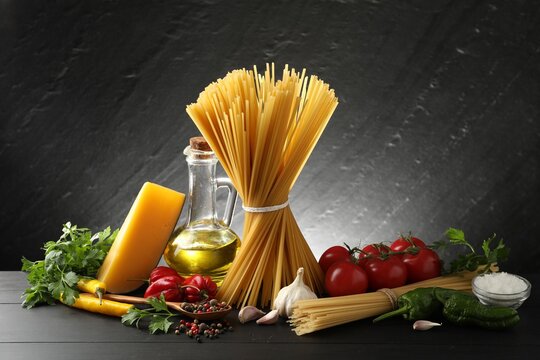 Raw spaghetti pasta, products and spices on black wooden table against dark textured background - Powered by Adobe