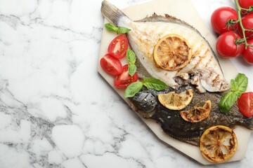 Homemade seafood dish. Tasty roasted flounder fish served with tomatoes, basil and lemon slices on white marble table, flat lay. Space for text