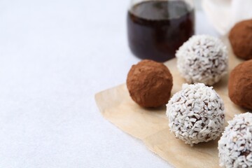 Delicious homemade candies with cocoa powder and coconut flakes on light table, closeup. Space for text