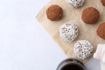 Delicious homemade candies with cocoa powder and coconut flakes on light table, flat lay. Space for text